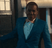 a man in a blue suit and pink bow tie stands in front of a door