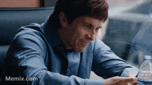 a man in a blue shirt is sitting at a table with a bottle of water and a memex.com logo