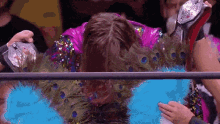 a wrestler wearing a peacock feather costume is being congratulated by his opponent