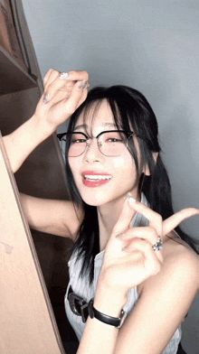 a woman wearing glasses and a watch is making a heart shape with her fingers