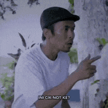 a man wearing a hat and a white shirt is pointing at something while talking .