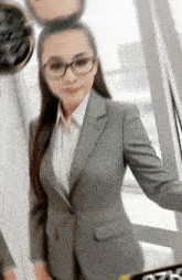 a woman in a suit and glasses is standing in front of a window in an office .