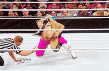 two wrestlers are wrestling in a ring and one of them is wearing pink shorts