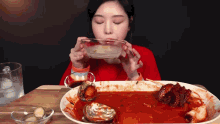 a woman is drinking from a glass bowl while eating a plate of food