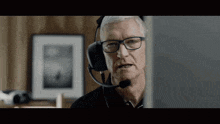 an older man wearing glasses and a headset looks at a computer screen