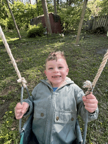 a young boy is smiling while sitting on a swing outside
