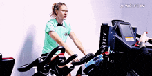 a woman in a green shirt is riding an exercise bike with a wolfe tv logo in the background