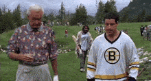 a man in a boston bruins jersey is standing on a golf course next to a man in a floral shirt .