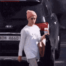 a woman wearing a pink beanie and a white shirt is walking down the street holding a cup of coffee .