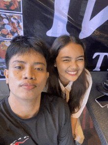 a man and a woman pose for a picture in front of a sign that says t