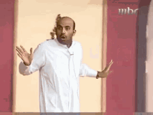 a bald man in a white shirt is standing in front of a pink wall with his arms outstretched .