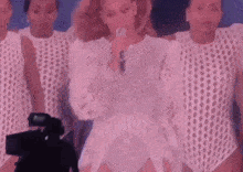 a woman is singing into a microphone in front of a camera