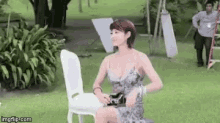 a woman in a dress is sitting on a white chair in the grass .