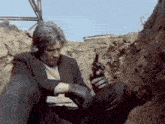 a man in a suit and gloves is holding a gun in a trench
