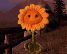 a stuffed sunflower with a smiling face is standing next to a wooden fence