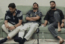 three men are sitting on a green couch .