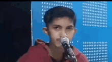 a young boy is singing into a microphone while wearing a red hoodie .