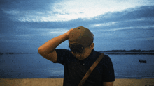 a man wearing a baseball cap is standing in front of the ocean