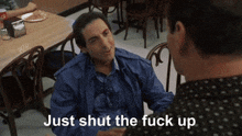 a man in a blue jacket is talking to another man in a restaurant and the man is saying just shut the fuck up