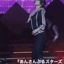 a woman in a black jacket and hat is dancing on a stage with a purple background and the word stars on the bottom