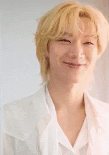 a young man with blonde hair and a white shirt smiles for the camera