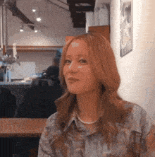 a woman with red hair and a pearl necklace is sitting at a table and smiling .