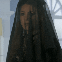 a woman wearing a black veil is standing in front of a window
