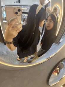 two women are taking a selfie in a mirror with one wearing a bunny headband