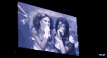 a couple of women are singing into microphones on a large screen .