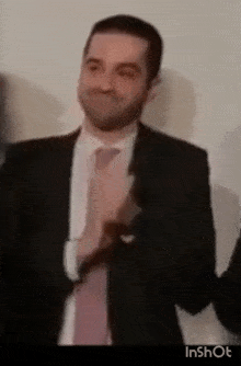 a man in a suit and tie is clapping his hands in a blurry video .