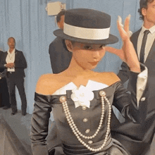 a woman wearing a hat and a pearl necklace is making a peace sign .