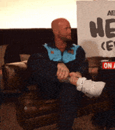 a man is sitting on a couch in front of a sign that says " he "