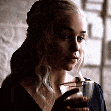 a woman is holding a glass of wine in her hand and looking at the camera .