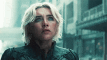 a woman with blonde hair and blue eyes is wearing a black jacket and looking up .