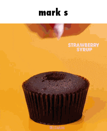 a chocolate cupcake with strawberry syrup being poured on top