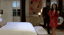 a man in a black jacket and a woman in a red coat are standing in a bedroom
