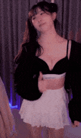 a woman in a black bra and a white skirt is dancing on a webcam .