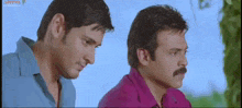 two men are standing next to each other looking at something .