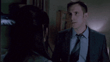 a man in a suit talks to a woman in a dark room