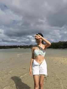 a woman in a bikini top and white shorts stands on a beach