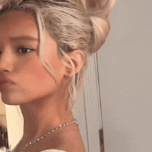 a close up of a woman 's face with blonde hair in a bun