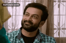 a man with a beard wearing a plaid shirt is smiling .