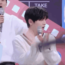 a man holding a microphone in front of a take sign
