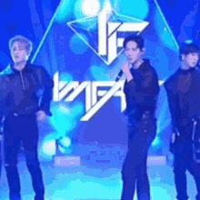 a group of men are standing on a stage holding microphones and singing into them .