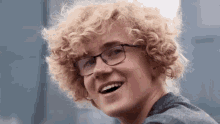 a young man with curly hair and glasses is laughing .