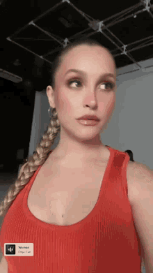 a woman in a red tank top with a braided ponytail is looking at the camera