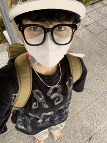 a person wearing a mask and glasses has a black shirt with whales on it and a backpack on their back