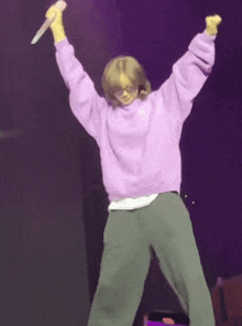 a woman in a purple sweatshirt is holding a microphone in her hand