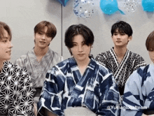 a group of young men wearing kimonos are sitting next to each other in front of balloons .