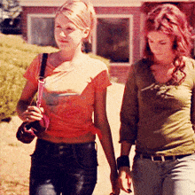 two women are walking down a street holding hands and one is wearing an orange shirt